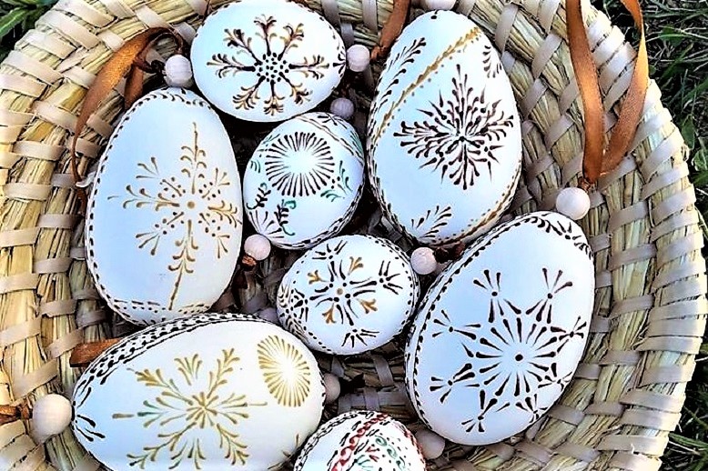 Białe jajka w słomianym koszyku pomalowane w brązowe wzory.