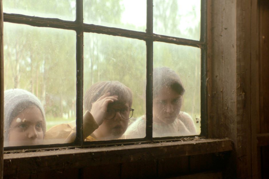 Dwójka dzieci zagląda przez okno do wnętrza budynku.