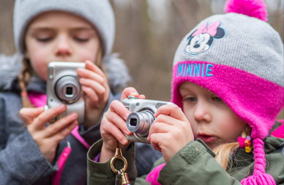 Dwójka małych dzieci w zimowych ubraniach trzyma w rękach aparaty fotograficzne.