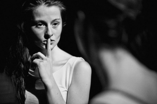 Czarno-białe zdjęcie młodej kobiety trzymającej palec na ustach. Ciemne tło.