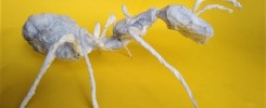 Biała papierowa rzeźba mrówki. Żółte tło.