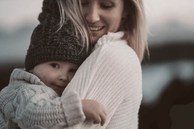 Uśmiechnięta kobieta trzyma na rękach uśmiechnięte dziecko.